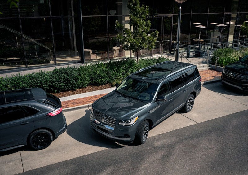 A 2023 Lincoln Navigator® SUV is being parallel parked between two vehicles on a downtown street outside of a luxury hotel. | Haldeman Lincoln in Allentown PA
