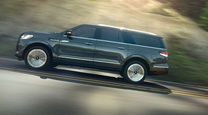 A 2023 Lincoln Navigator SUV being driven on a freeway bathed in sunlight.