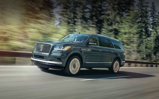 A Lincoln Navigator SUV is being driven on a tree-lined road