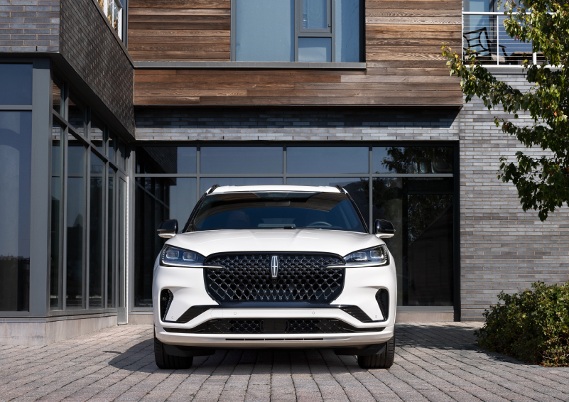 A white 2025 Lincoln Aviator® SUV is shown parked outside a modern building with gray brick and wood accents. | Haldeman Lincoln in Allentown PA