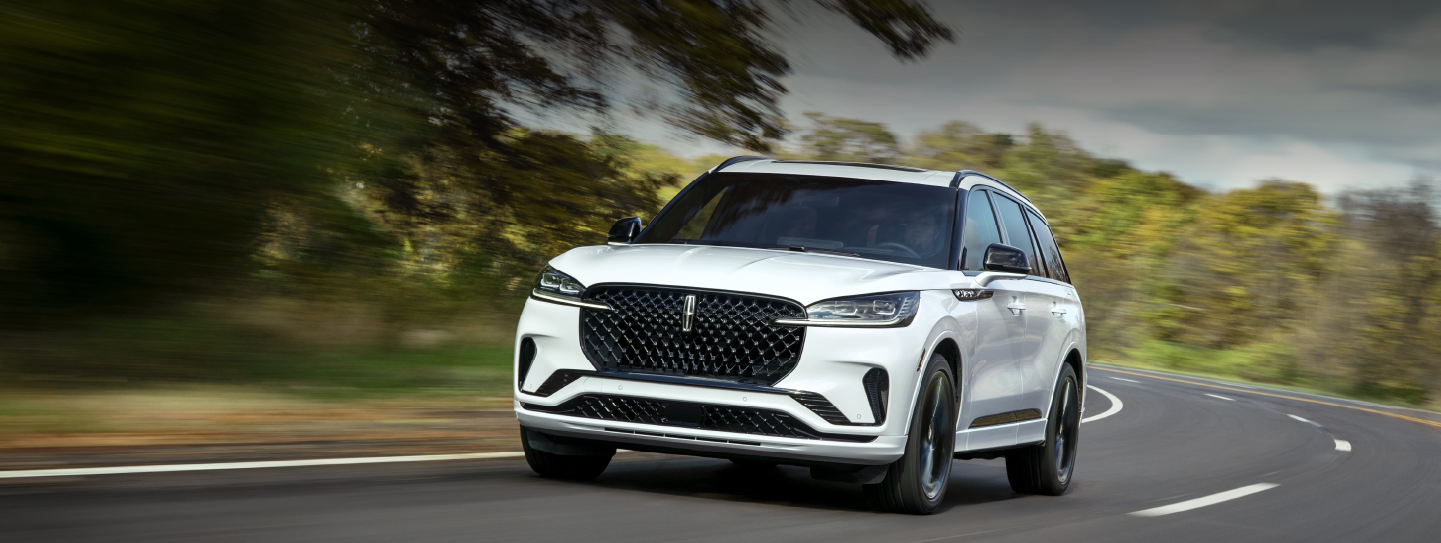 A white 2025 Lincoln Aviator® SUV is being driven down a road lined with trees. | Haldeman Lincoln in Allentown PA