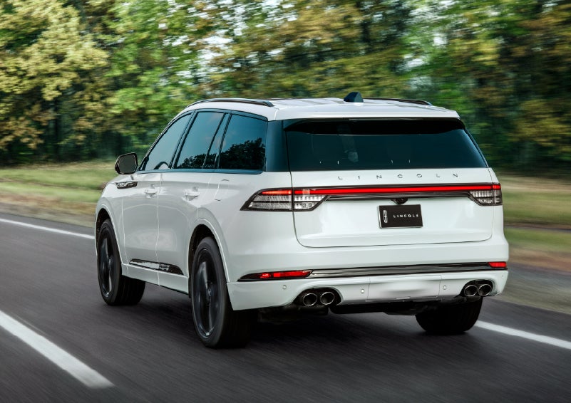 A white 2026 Lincoln Aviator® SUV is being driven away down a road lined with colorful trees. | Haldeman Lincoln in Allentown PA