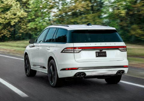 A white 2026 Lincoln Aviator® SUV is being driven away down a road lined with colorful trees. | Haldeman Lincoln in Allentown PA