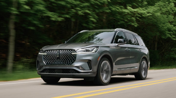 A 2027 Lincoln Aviator® SUV is being driven down a road lined with trees. | Haldeman Lincoln in Allentown PA